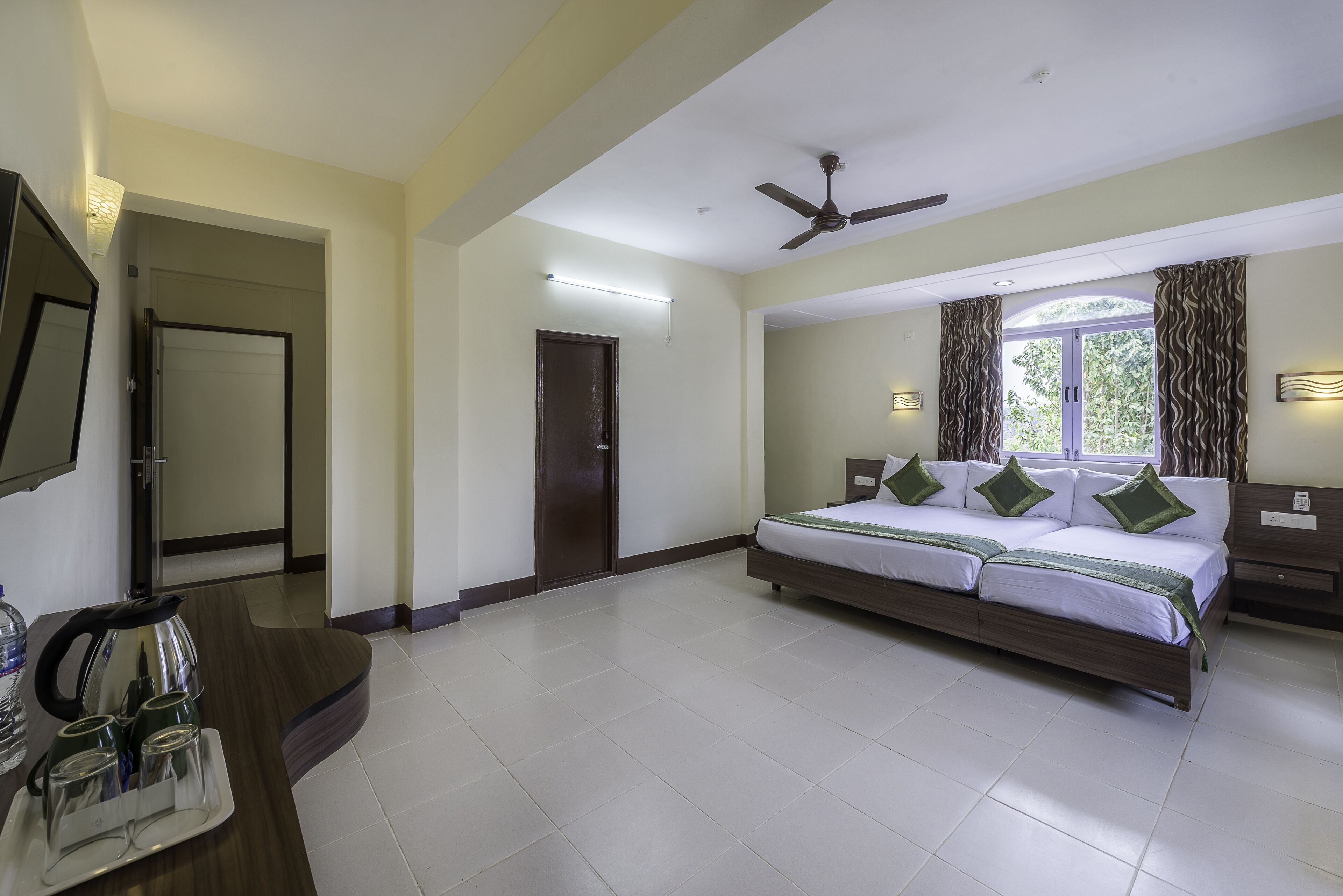 Habitación de hotel con cama, escritorio, ventilador de techo y ventana con cortinas.