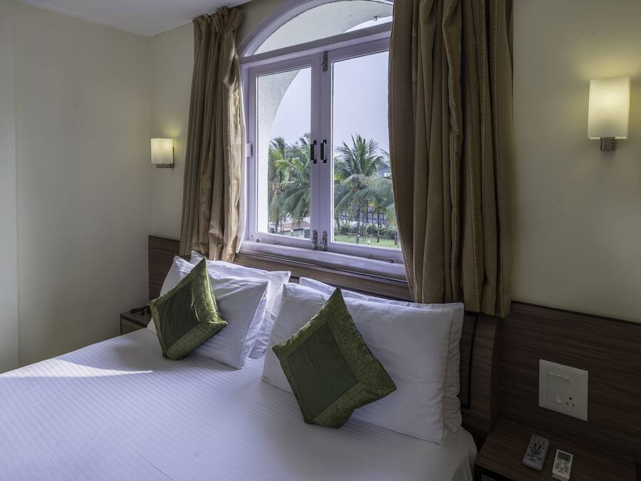 A hotel room with a bed, two pillows, a nightstand with a remote, and a window with curtains.