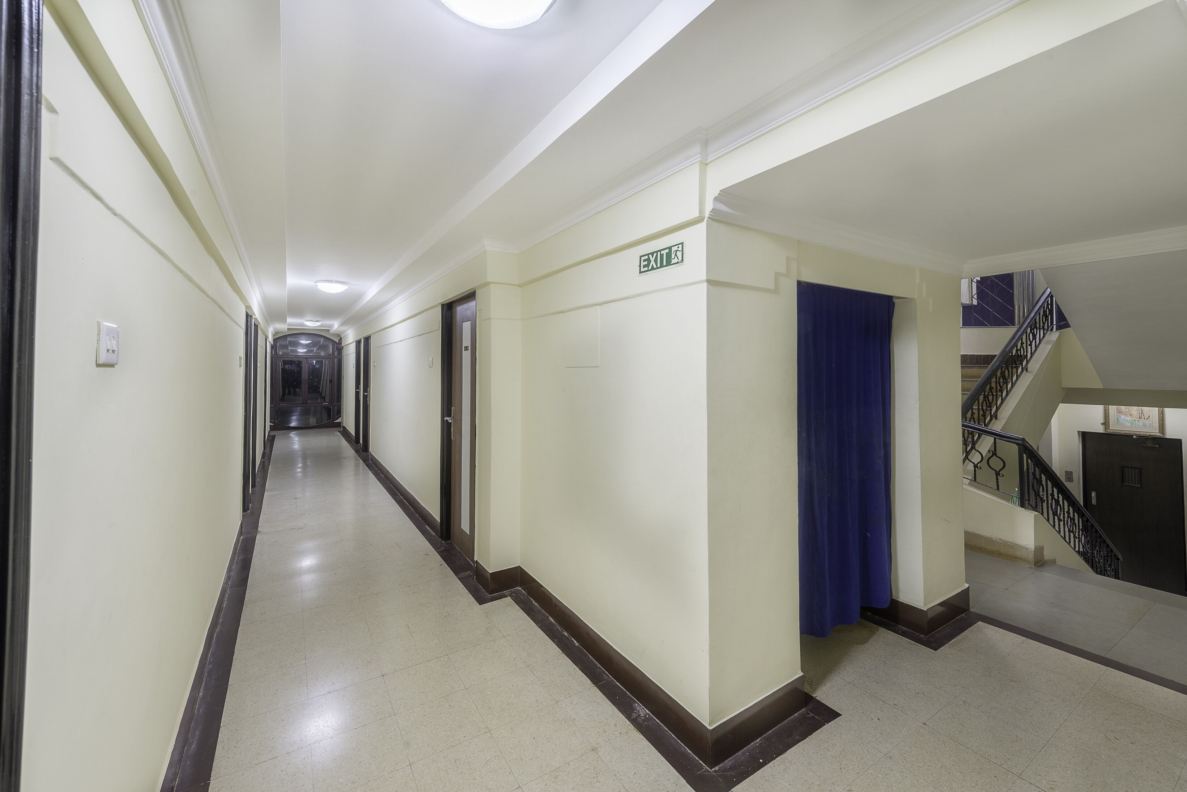 A long, narrow hallway with a sign indicating an exit, a blue curtain, and a staircase on the right.