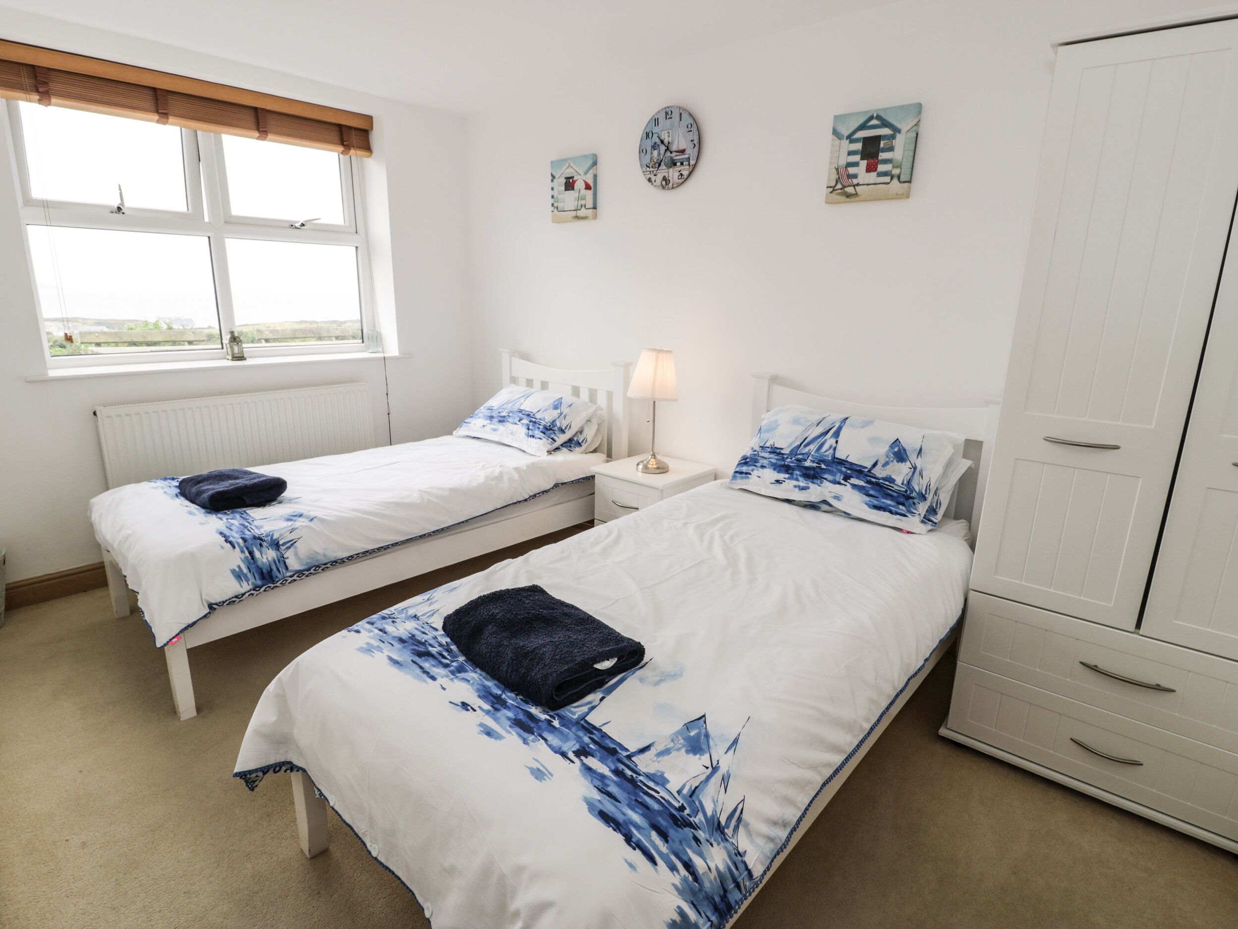 Een kamer met twee eenpersoonsbedden, een nachtkastje met lamp, een radiator, een raam met zonwering en een kledingkast.