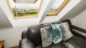A room with a black leather sofa, two skylights, and a view of a green landscape. - Bwthyn Awel (Holyhead)