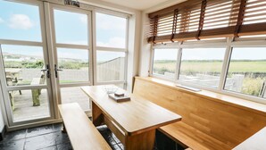 A room with a wooden bench, a table, and a view of the outdoors through large windows. - Bwthyn Awel (Holyhead)