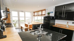 A modern kitchen with a central island, stainless steel appliances, and a view to the outside. - Bwthyn Awel (Holyhead)
