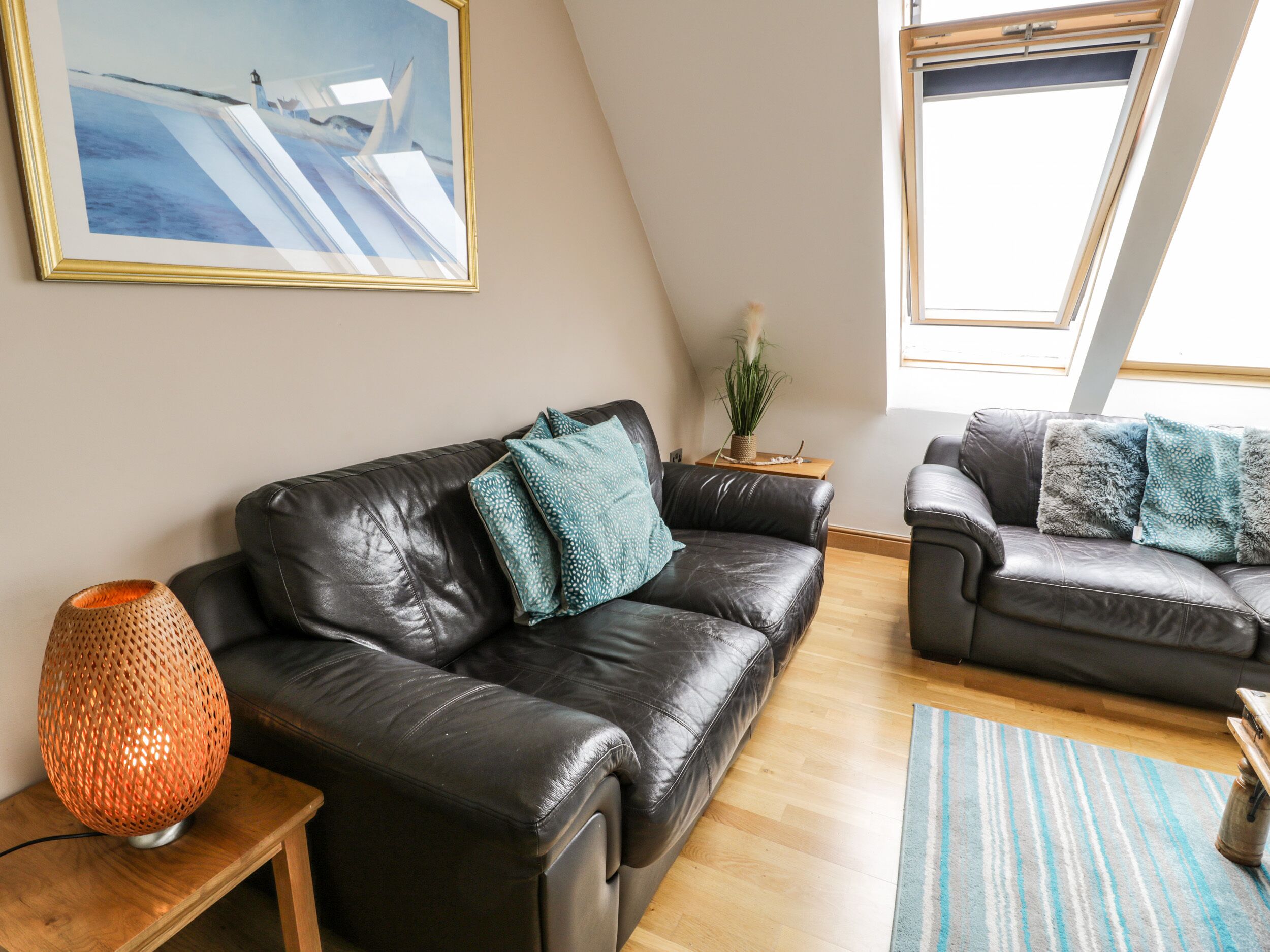 A modern living room with two black leather sofas, a wooden side table, a floor lamp, and a painting on the wall.