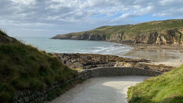A coastal path leading to a beach with a stone wall and grassy areas. - Bwthyn Awel (Holyhead)