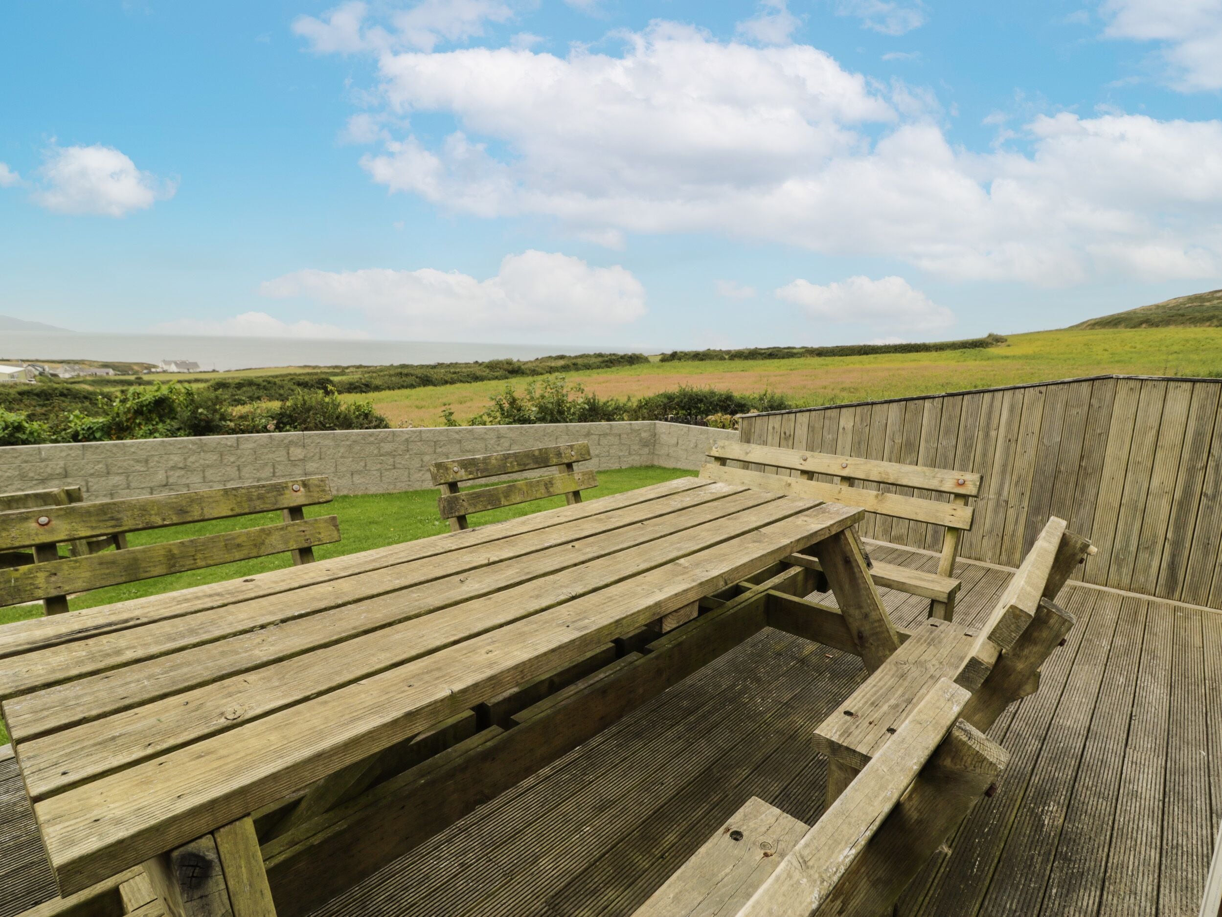 Une terrasse en bois avec des bancs, donnant sur un champ verdoyant et un mur de pierre.