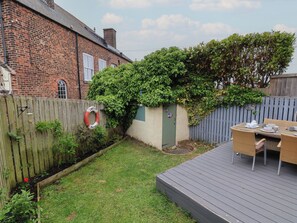 Un patio trasero con una casa de ladrillo, una terraza de madera y un pequeño jardín.