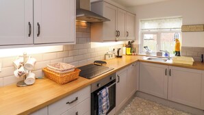 A modern kitchen with white cabinets, a stainless steel range hood, and a window with a view of the outside. - Over Esk (Whitby)