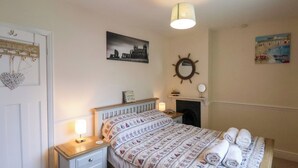 A bedroom with a bed, bedside table, lamp, wall art, and a fireplace. - Over Esk (Whitby)