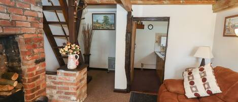 A cozy living room with a brick fireplace, a brown leather sofa, and a wooden ceiling.