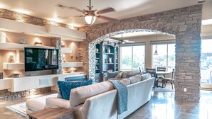 A modern living room with a stone accent wall, a flat-screen TV, a sofa, and a dining area. - Enjoy quality time in beautiful Fountain Hills at the coziest home (Fountain Hills)