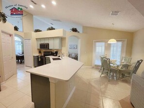 A spacious kitchen with a central island, a dining area with a round table and chairs, and a living room with a sofa.