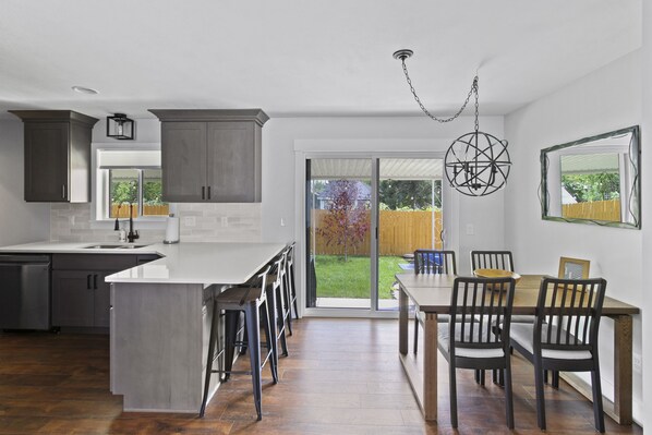 A modern kitchen with a large island, dark wooden cabinets, and a dining area with a wooden table and chairs. - Monthly Special! Location! New Everything 5 Bed Home w/ Hot Tub (Salt Lake City)