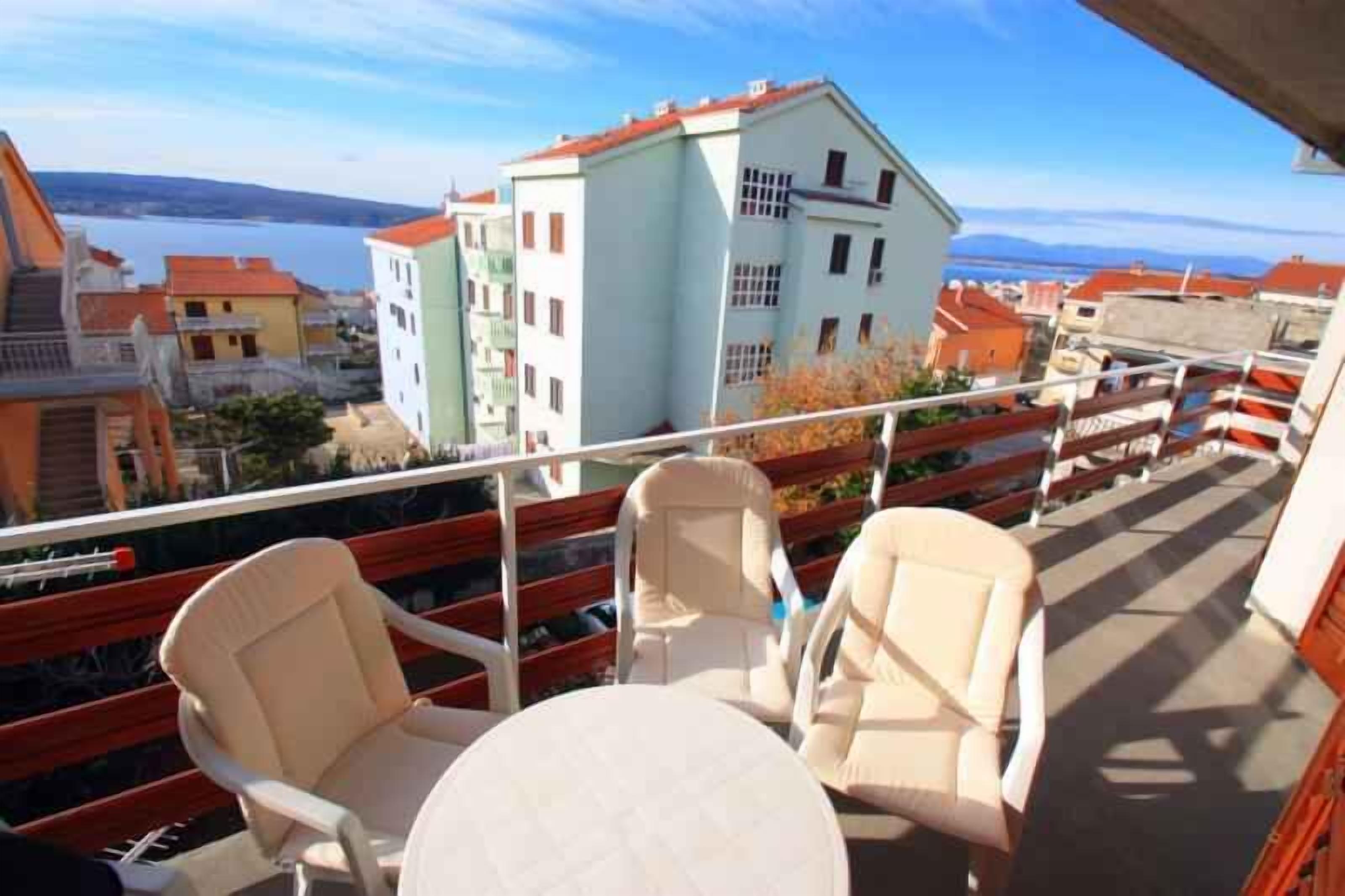 Ein Balkon mit zwei Stühlen und einem Tisch, der auf eine Stadtansicht mit Gebäuden und einem Gewässer blickt.