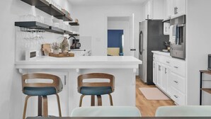 Una cocina moderna con armarios blancos, una isla central con taburetes y estanterías empotradas con cristalería.