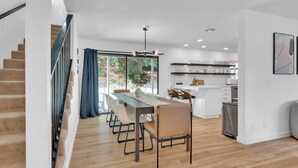 A modern kitchen with white cabinets, a dining area with a wooden table and chairs, and a staircase with a blue curtain. - Large Pool l Hot Tub l Spacious l Family Friendly (Atascadero)