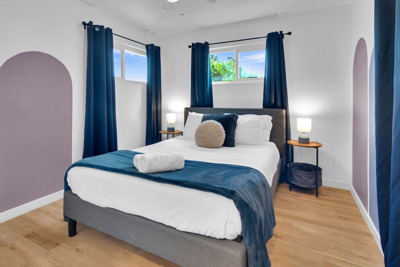 A modern hotel room with a large bed, two bedside tables with lamps, and a view of the outdoors through a window.