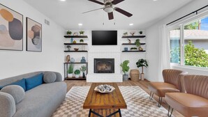 Una sala de estar moderna con chimenea, ventilador de techo y un ventanal grande.