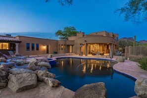 A modern house with a swimming pool surrounded by rocks, a patio with outdoor furniture, and a well-lit interior. - Luxurious Equestrian Villa in Scottsdale (Scottsdale)