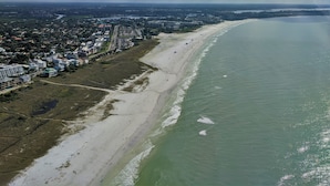 Luftaufnahme einer Küstenstadt mit breitem Strand, Wohngebieten und einer großen Wasserfläche.