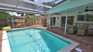 Ein Schwimmbad mit überdachtem Patio, Gartenmöbeln und einem Deckenventilator.