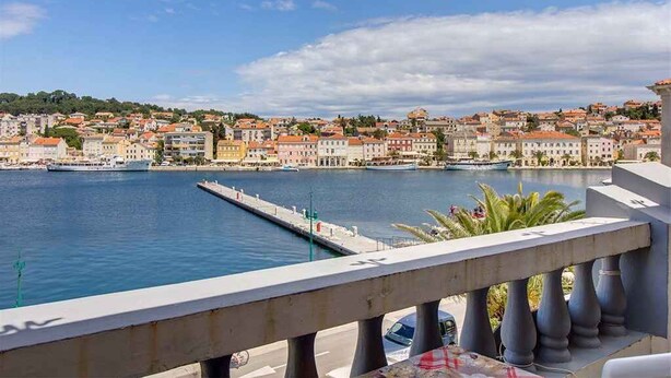 Paisagem costeira com um porto de iates, edifícios com telhados de terracota e céu claro.