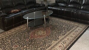 Ett vardagsrum med två svarta lädersoffor, ett soffbord i glas, en mönstrad matta och ett litet bord med en lampa.