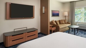 Habitación de hotel con una cama grande, un televisor de pantalla plana en la pared, un aparador de madera, un sofá, una mesita y una ventana con cortinas.