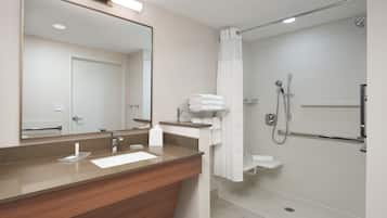 A modern bathroom with a wooden vanity, a large mirror, a shower with a handheld showerhead, and a towel rack.