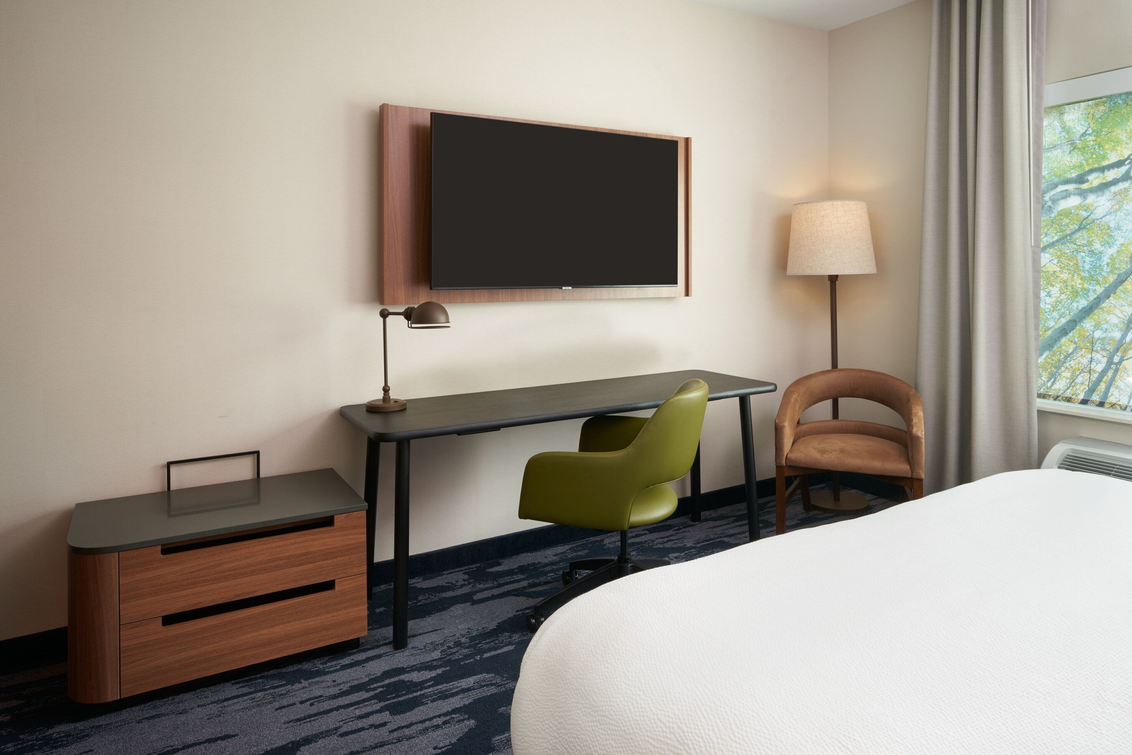 Une chambre d’hôtel comprenant un lit, un bureau avec une chaise, un téléviseur fixé au mur et une lampe.