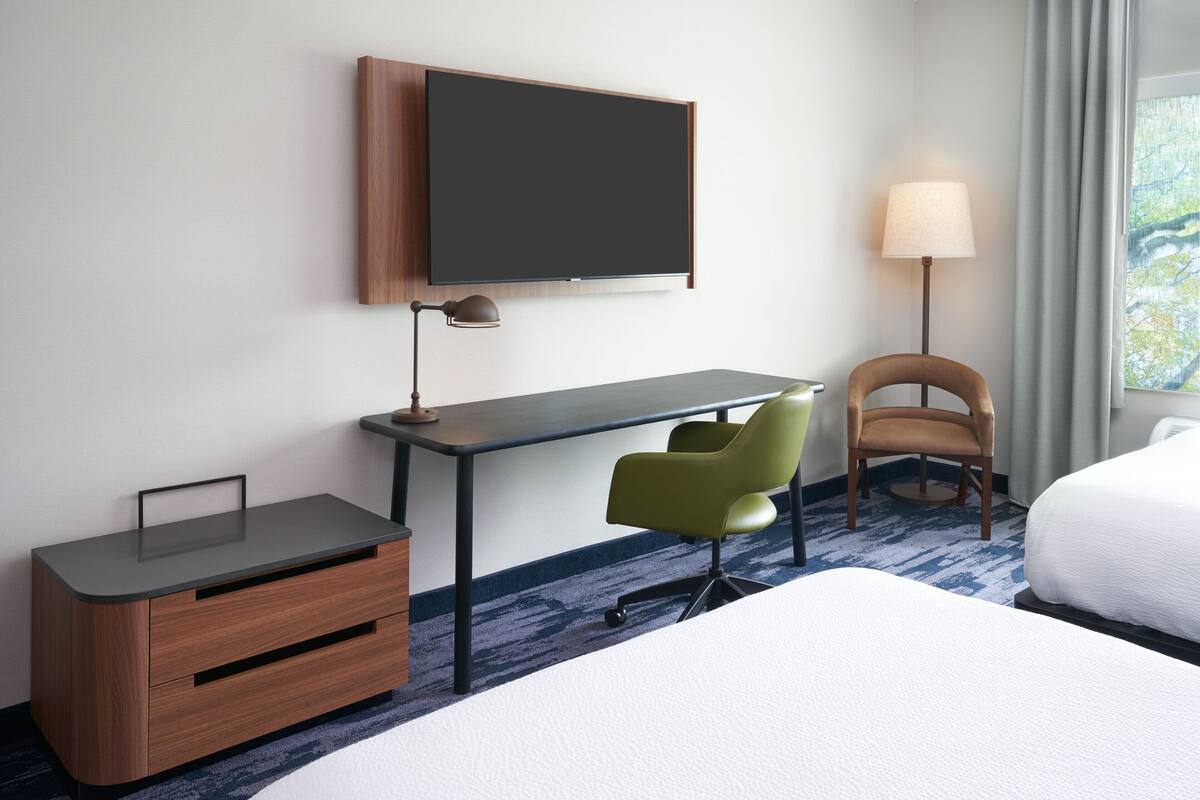 Una habitación de hotel con cama, escritorio, silla, televisor y lámpara.