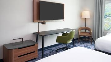 A hotel room with a bed, a desk with a chair, a television, and a lamp.