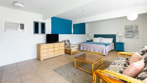 Una habitación de hotel moderna con una cama, televisión, cómoda de madera, silla de mimbre y una pequeña mesa.