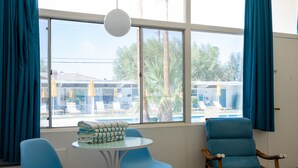 A room with a large window, a table with folded towels, two blue chairs, and a wooden chair.