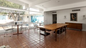 A spacious dining area with a wooden table and chairs, large windows, and a view of the outdoors.
