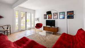 A living room with a red sofa, a glass coffee table, a red chair, a TV on a wooden cabinet, and a door with glass panels.