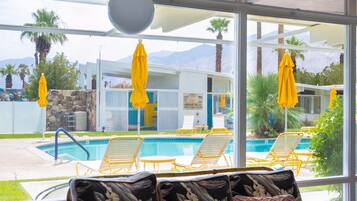 Un espace aménagé au bord de la piscine, avec des parasols jaunes, des chaises longues et une vue sur une chaîne de montagnes.