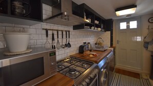 A kitchen with a microwave, stove, and oven. There are utensils hanging on the wall and a toaster on the counter. - Matchbox is a delightful dog-friendly cottage in Winchelsea, East Sussex (Winchelsea)