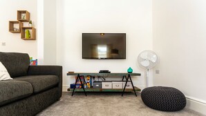 Ein Wohnzimmer mit einer Couch, einem Fernseher, einem kleinen Tisch mit Stauraum, einem Ventilator und einem Sitzsack.