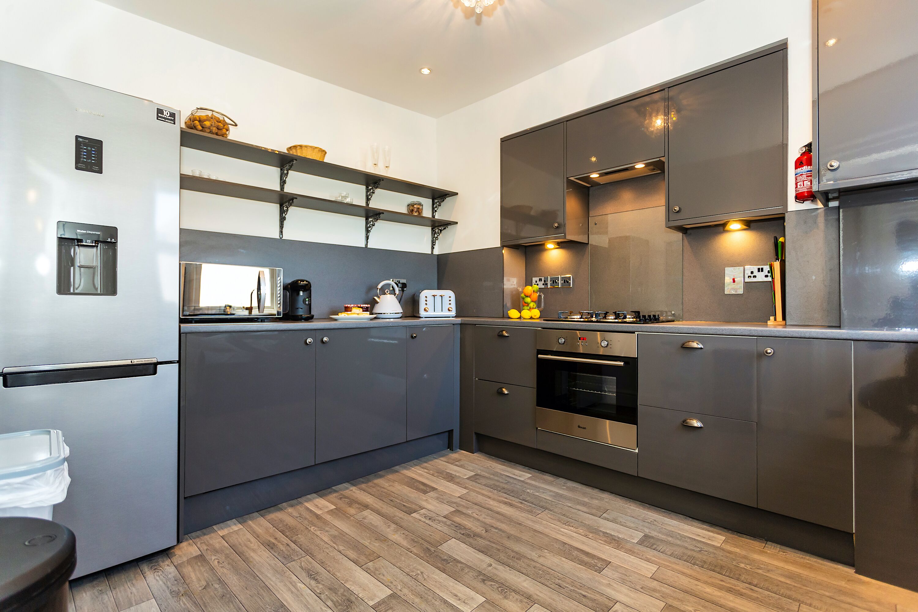 A modern kitchen with stainless steel appliances, wooden flooring, and built-in shelves.