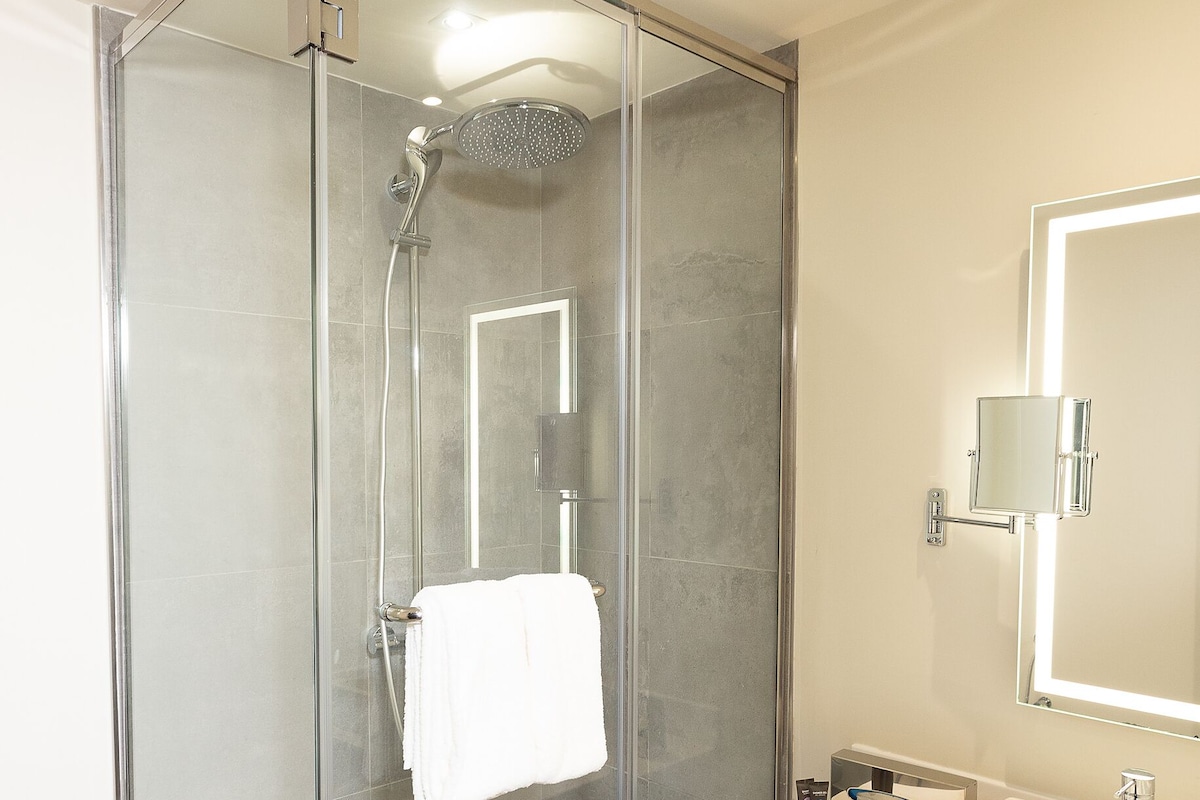 A modern bathroom with a glass-enclosed shower, a white sink, and a large mirror.