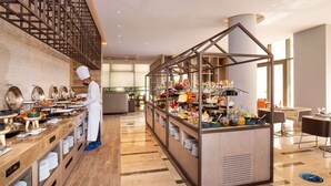 A modern hotel restaurant with a chef preparing food, a buffet with various dishes, and a seating area with tables and chairs. - Novotel Tunis Lac (Tunis)