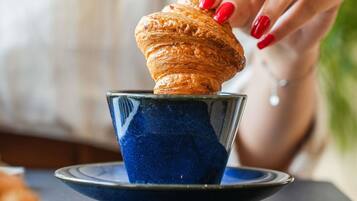 Eine Hand hält einen Croissant über einer blauen Keramiktasse.