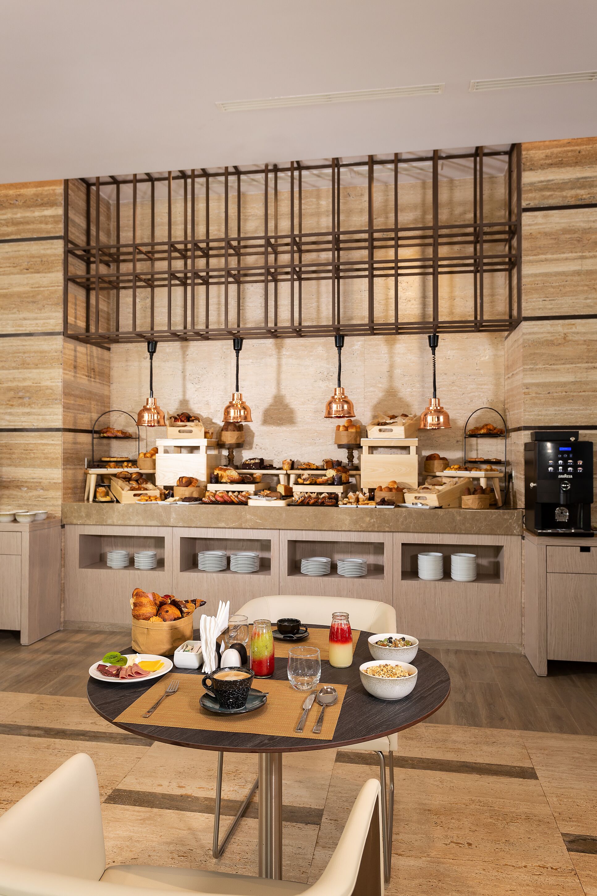 Disposição de buffet de café da manhã com diversos alimentos, um espaço para café e uma máquina de café.