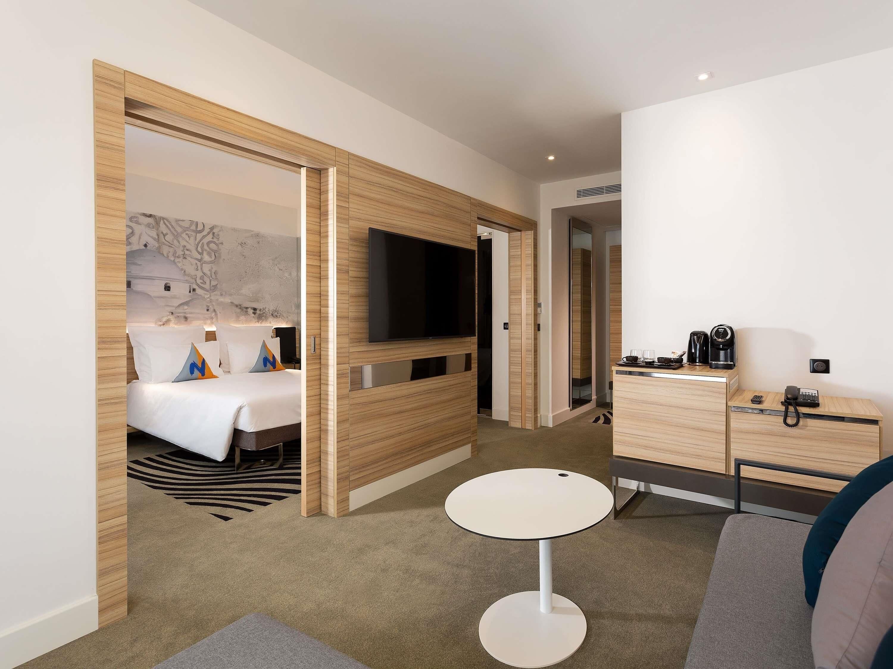 A modern hotel room with a bed, a TV, a desk with a phone, and a small round table.