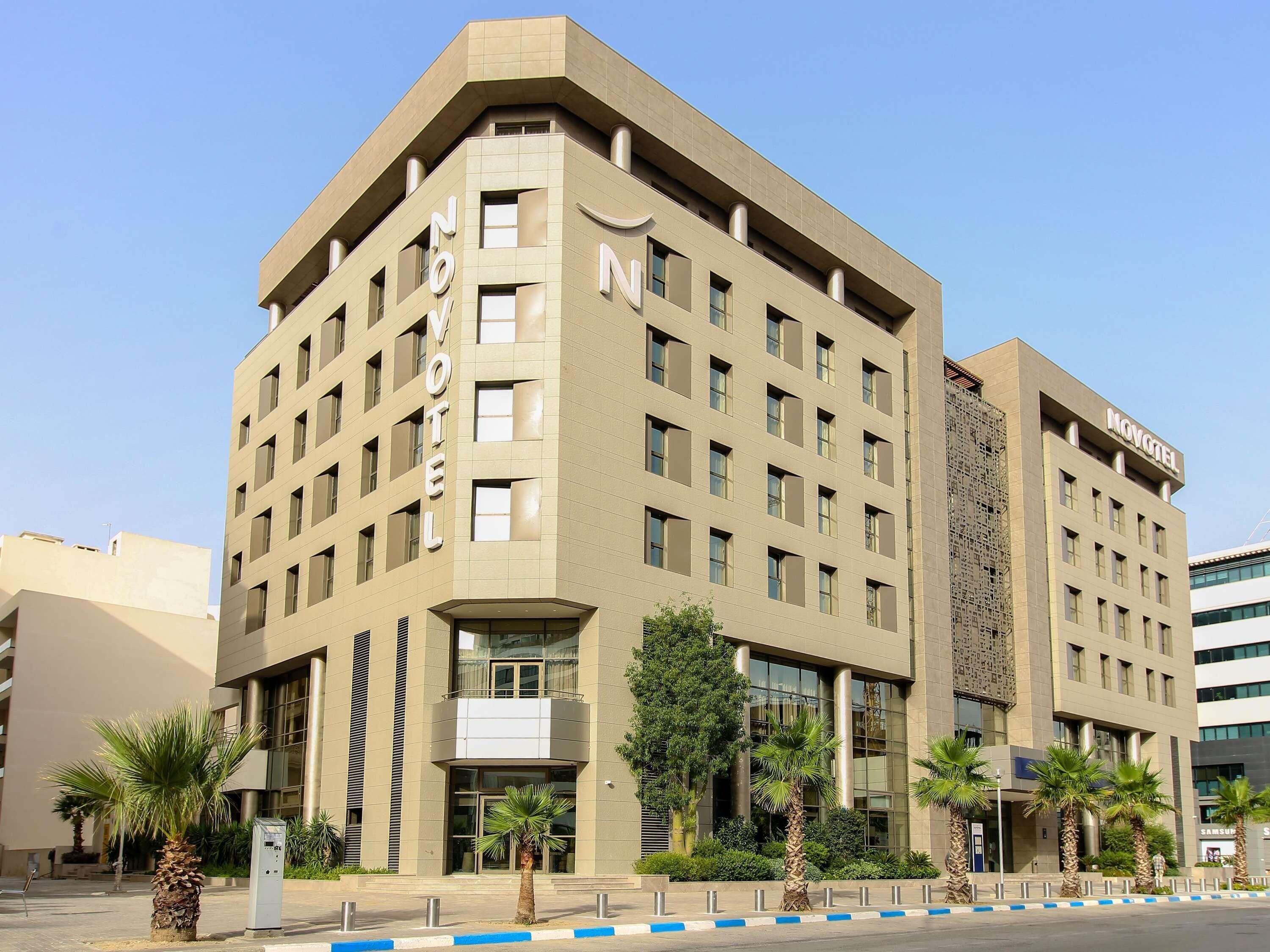 A modern hotel with a beige facade, multiple floors, and a prominent 'NOVOTEL' sign.