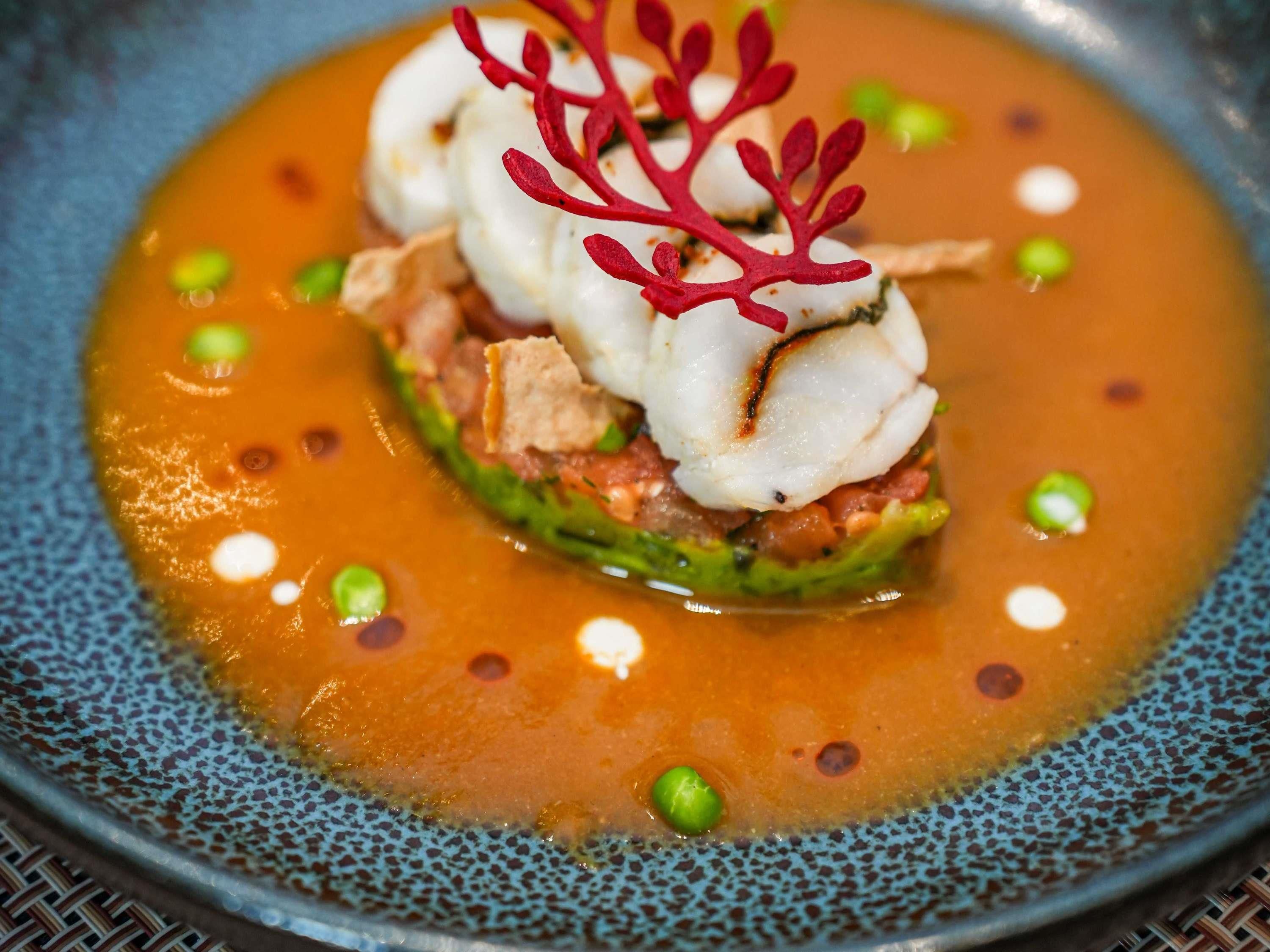 A dish with seafood, vegetables, and a decorative red element on a speckled blue plate.