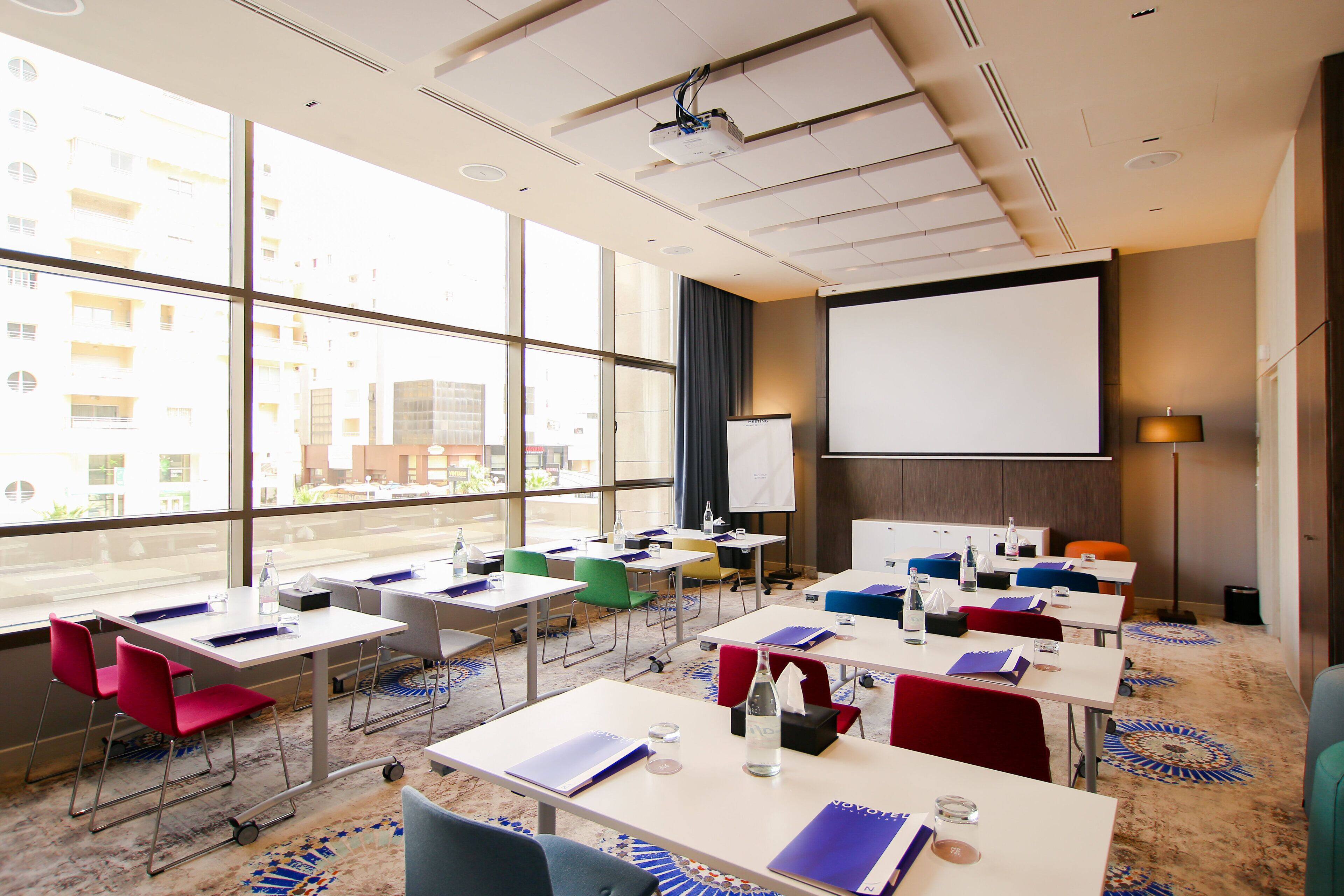 A conference room with multiple tables, chairs, a projector, and a large screen.