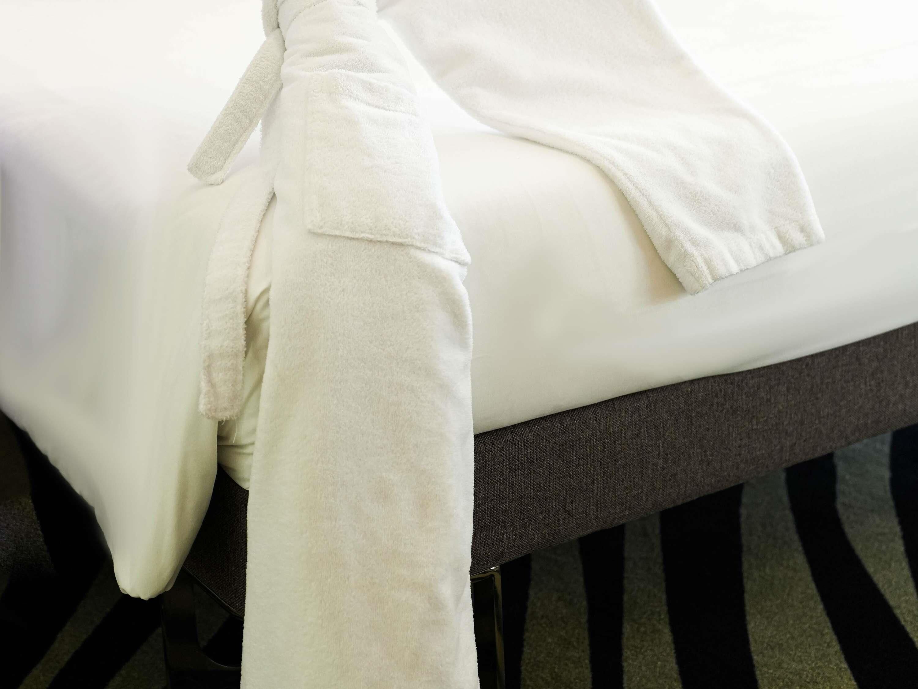 Una cama bien hecha con una manta blanca y una bata blanca sobre ella.