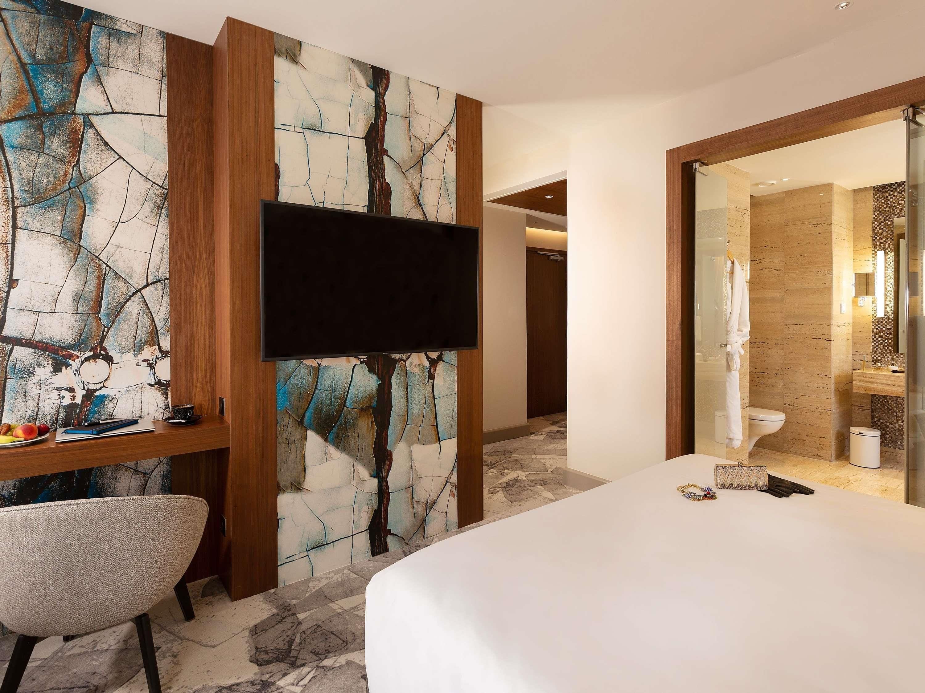 Habitación de hotel con cama, escritorio con silla, televisión de pantalla plana y baño con espejo y retrete.